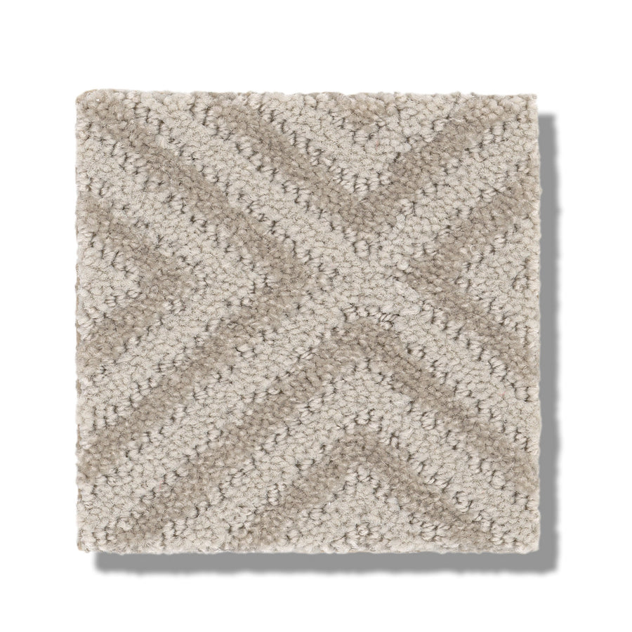 A square swatch of Aristocrat On Trend Carpet in beige and light brown, featuring a chevron or diamond pattern with raised, looped fibers and a matte finish. The swatch is shown casting a shadow on a white background.