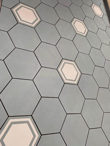 The 8x9 Glazed Hex Tile features a grid of mostly solid gray tiles, with select pieces showcasing white and light gray concentric hexagons for a stylish accent that suits modern living spaces.