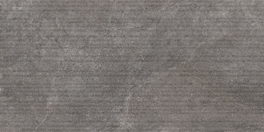 A close-up of the Santorini 12x24 Grooves Deco Porcelain Tile, showcasing its textured gray stone-effect surface with subtle cracks, speckles, and faint horizontal lines that mimic concrete or natural rock.