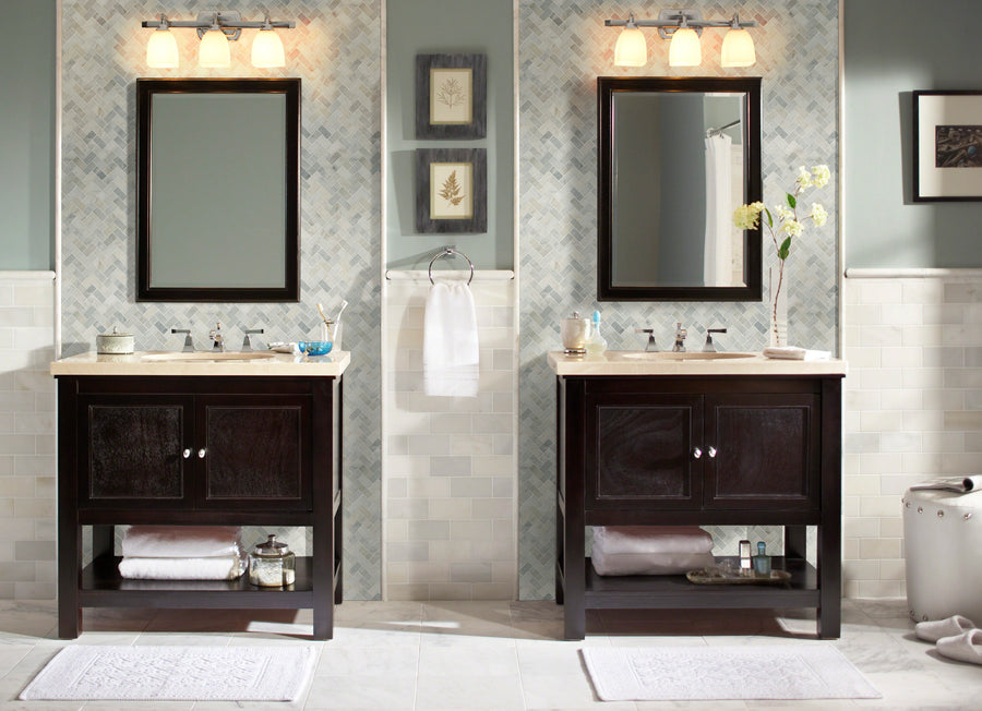 Modern bathroom with two dark wood vanities, mirrors, and lights above. White sinks, towels, and decor complement the light walls and floors featuring Arabescata Carrara Select 1x2 Herringbone Marble tiles.