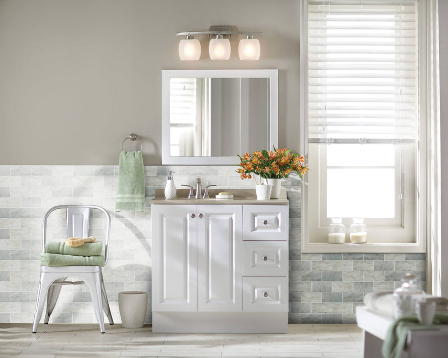 A bright bathroom with white cabinets, a large mirror, and flowers on the sink features soft walls and light gray Arabescata Carrara Select 3x6 Marble tile for a clean look. Blinds cover the window, while a metal chair holds neatly folded towels.