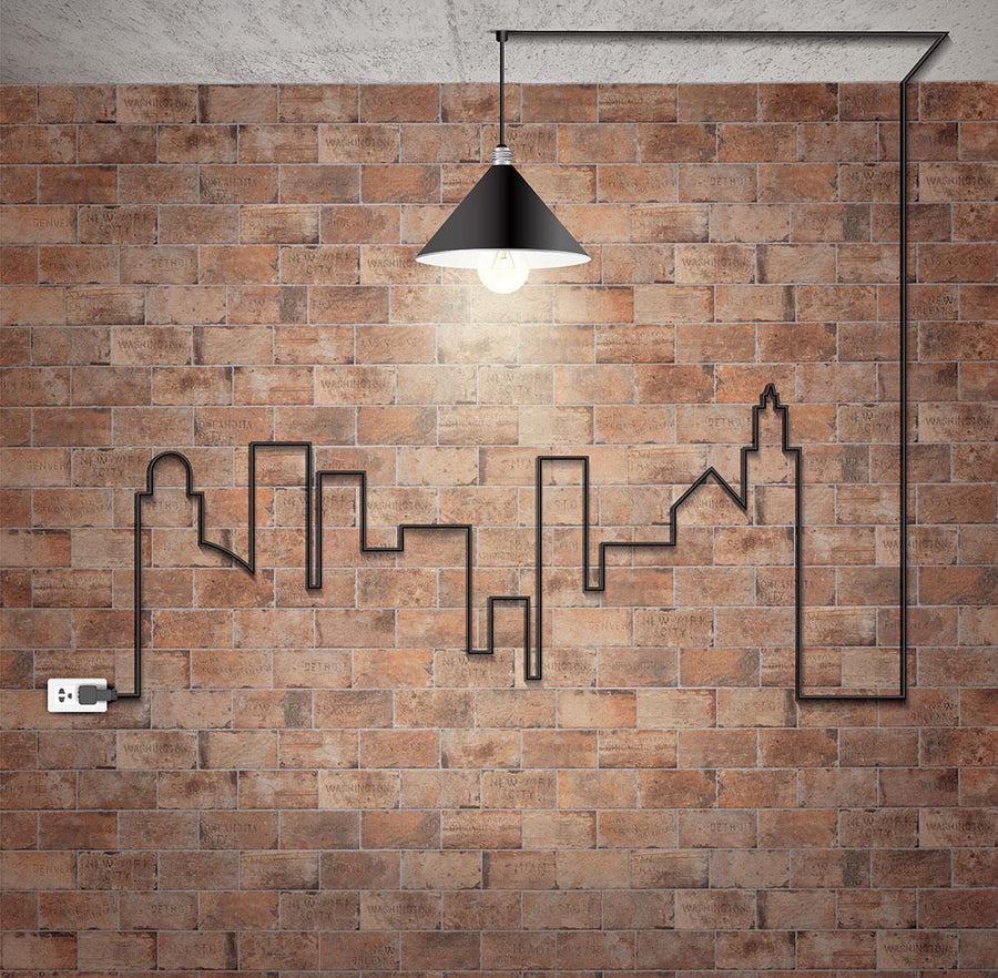 A black cord forms a city skyline on a vintage wall made of Chicago 4x8 Brick Tile, leading to a lit hanging pendant.