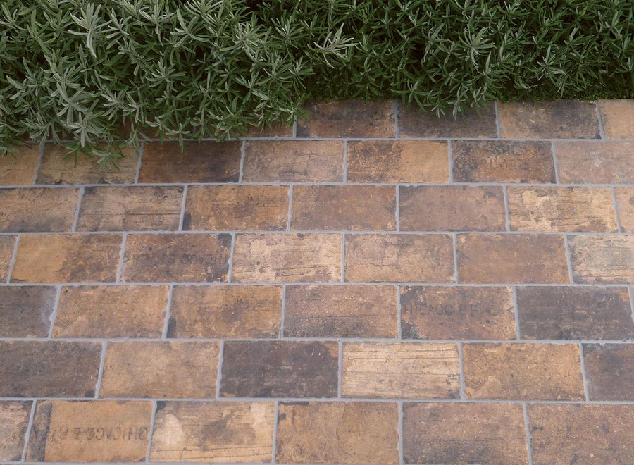 The Chicago 4x8 Brick Tile creates a timeless walkway, with lush plants in the background adding charm to any garden path.