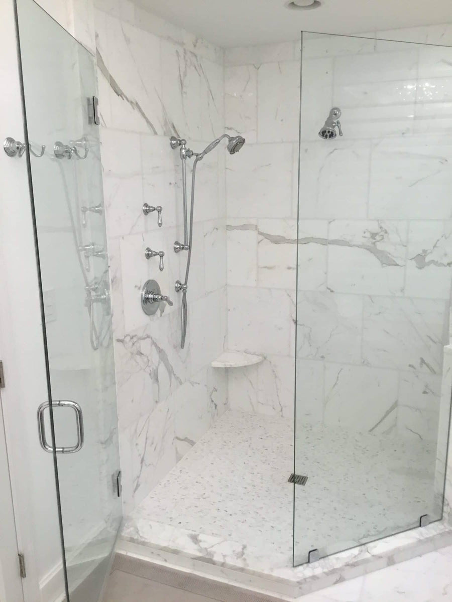 A modern walk-in shower with glass doors, Calacatta 18x18 Marble walls, a handheld showerhead, built-in corner shelf, and a tiled floor with a small square drain.