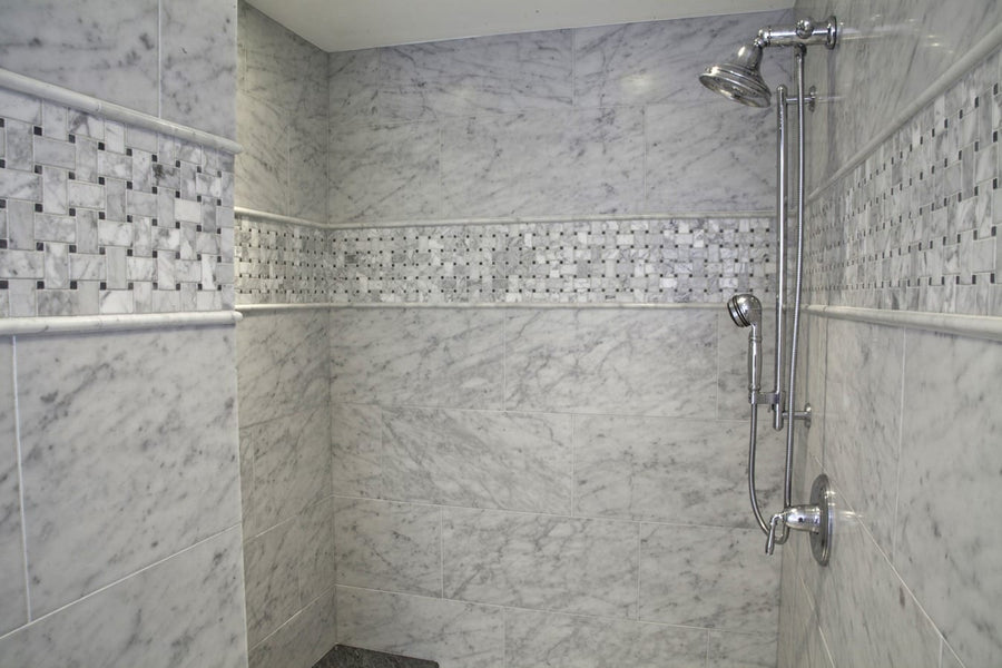 A modern shower featuring Carrara Select 12x24 Honed Marble tiles, a decorative mosaic border, and a chrome adjustable showerhead and faucet.