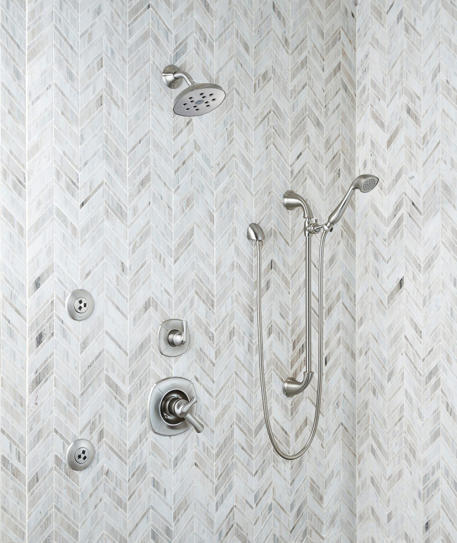Modern shower with a herringbone-patterned wall of Chevron Mosaic Natural Stone, featuring a rainfall and handheld showerhead with hose, multiple controls, and two wall-mounted jets. All fixtures are brushed metal.