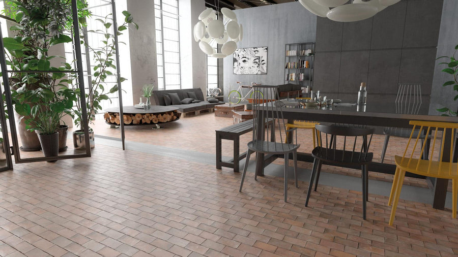 Modern loft apartment with large windows, Cottage 2.7 x 5.5 Brick Porcelain Tile flooring, tall plants, a dining area with mixed chairs, and a cozy living space featuring a gray sofa, wooden coffee table, bookshelves, and pendant lights.