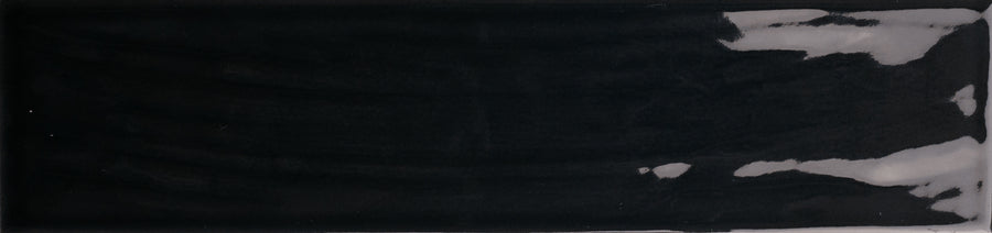 The Essence 2.5x10.5 Subway Tile is a rectangular black ceramic tile with a glossy, textured finish, featuring uneven white patches and reflections along the right edge.