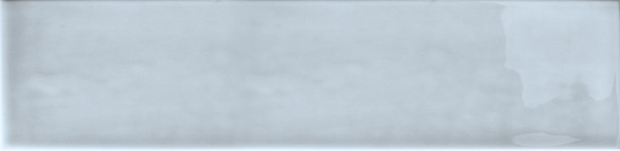The Essence 2.5x10.5 Subway Tile is a rectangular, light gray ceramic tile with a glossy, textured finish and slight shade variations, featuring subtle, irregular darker gray patches on the right edge.