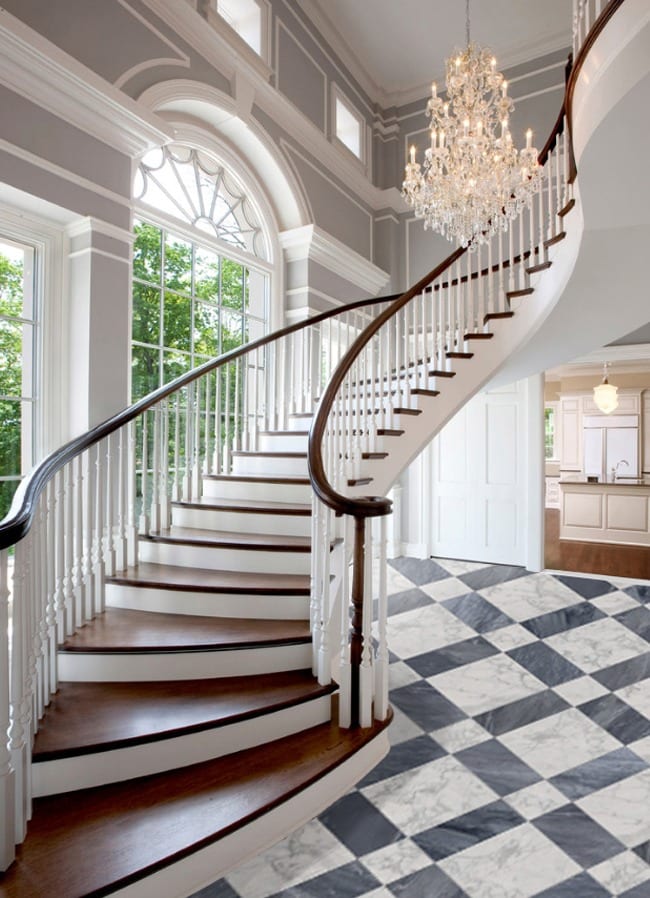 Elegant curved staircase with dark wood steps and white railings, arched window, crystal chandelier, and a black-and-white checkered Gioia Venatino 24x24 Marble floor in a spacious foyer.