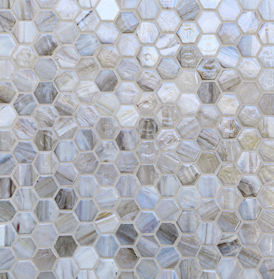 A close-up of Agate 1" Hex Pearl Finish Glass Tile shows small hexagonal tiles in white, gray, and beige tones, forming a mosaic pattern with a subtle pearl finish and glossy sheen.
