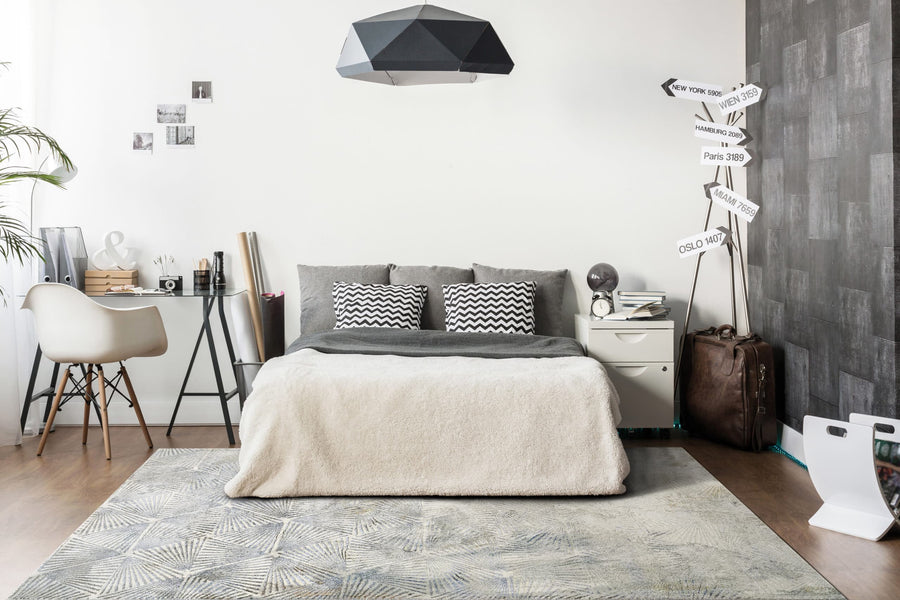 A modern bedroom with a double bed, gray and white bedding, geometric pendant light, desk and chair, wall art, suitcase, faux street sign, and the Gold 1355 Area Rug from Turkey adds subtle style to the gray and white decor.