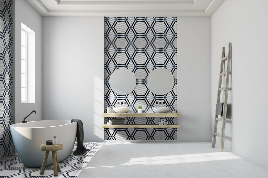 Modern bathroom features a white freestanding tub, wooden stool, and towel. Blue and white Evolve Hexagon Flower Mosaic Tile enhances the wall and floor. Double sinks, round mirrors, open shelves, and a wood ladder complete the design.