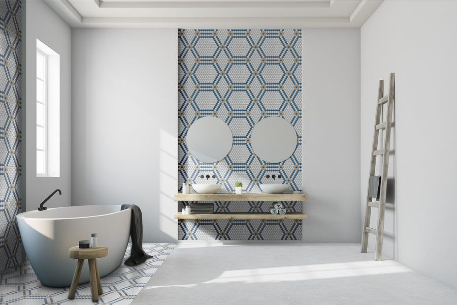 Modern bathroom with a freestanding bathtub, wooden stool, and towel. Behind dual sinks, blue Evolve Hexagon Flower Mosaic Tile creates geometric patterns, accented by round mirrors and wooden shelves. A wooden ladder leans against the right wall.