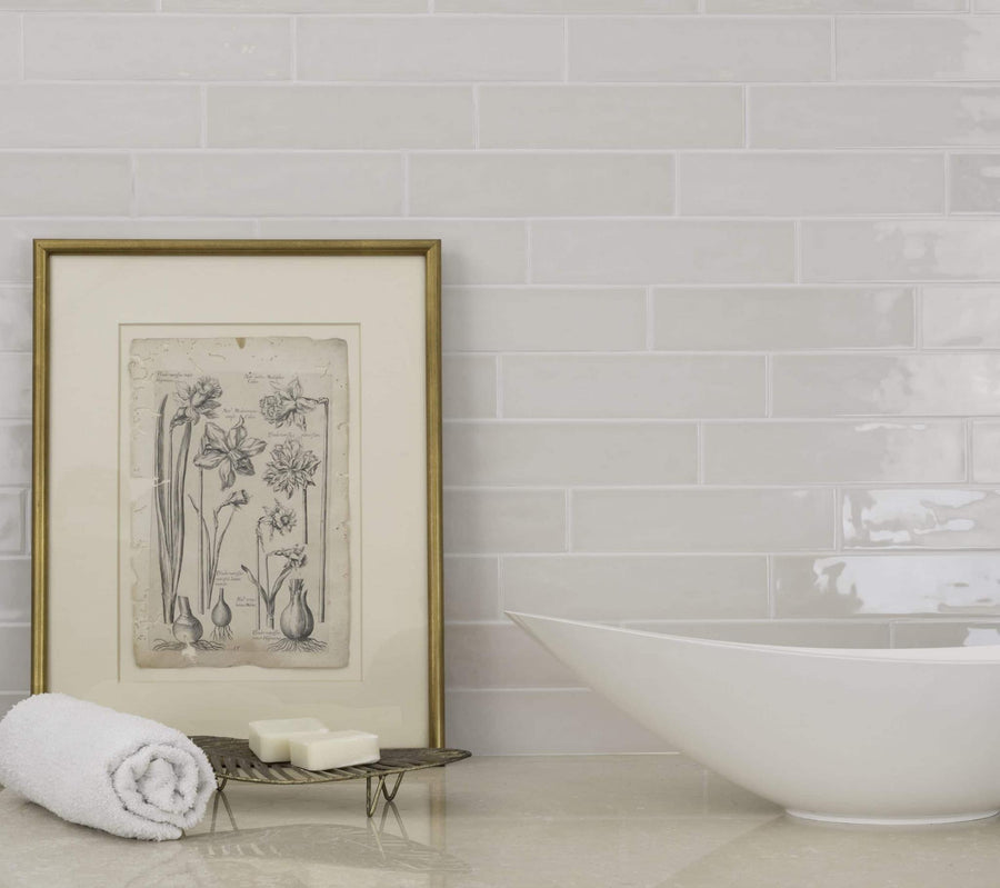 A bathroom countertop with a rolled white towel, two soap bars on a tray, a framed botanical print, and a modern white sink in front of a glossy Habitat 2.5x10.3 Subway Tile backsplash.
