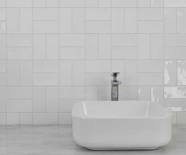 A modern white rectangular bathroom sink with a chrome faucet is set against a wall of Habitat 2.5x5.1 Subway Tile in a geometric pattern, with a light gray countertop that complements the stylish backsplash.