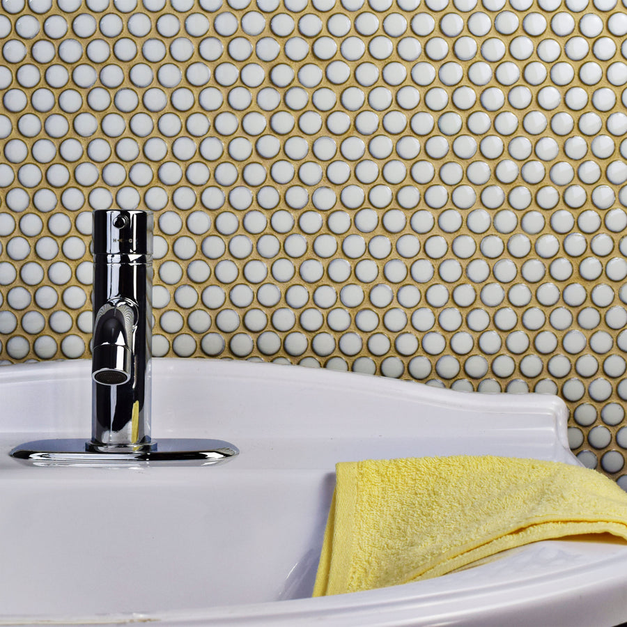 A chrome faucet sits on a white sink with a yellow towel, set against a wall of Hudson Penny Round Tile that adds subtle texture and charm to the scene.