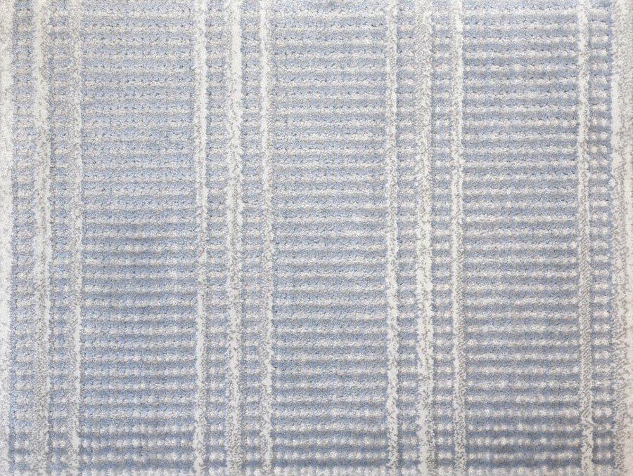 The Jazabella On Trend Carpet features a light blue and white geometric striped pattern with a subtle grid design. Custom finished and stain resistant, it offers everyday durability.