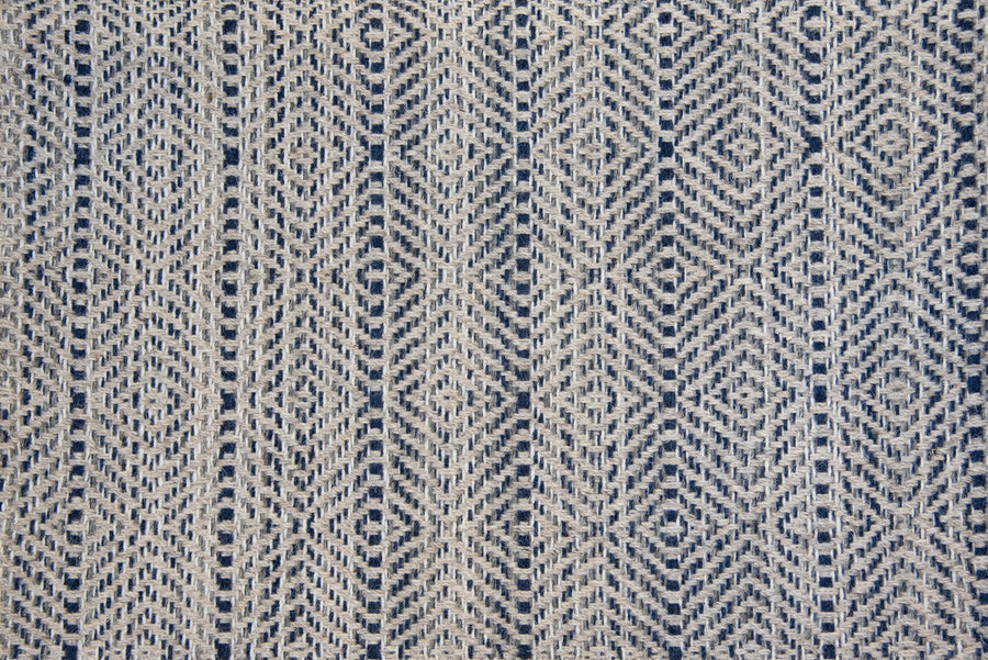 A close-up of the Kariba On Trend Wool Carpet highlights its blue and beige woven fabric, featuring a geometric diamond pattern with vertical lines and a textured, intricate finish.