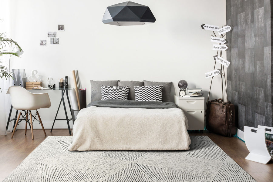 Modern bedroom featuring a neatly made bed, geometric-patterned pillows, and desk. The Lotus 8144 Area Rug adds durable high-low texture, complementing monochrome tones and minimalist decor for a cozy, stylish vibe.