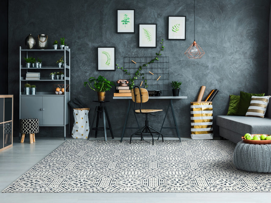 A modern home office features a gray high-low texture wall, a desk with plants, leaf art prints, the Lotus 8149 Area Rug for durability, metal shelves, a gray sofa, and geometric decor with green accents.