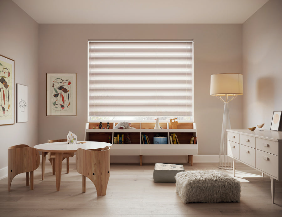A cozy, modern kids’ room with light wood furniture, a round table, two chairs, a fluffy rug, and a low bookshelf under a large window featuring Modern Precious Metals® Aluminum Blinds for ideal light control. Soft neutrals and framed art complete the look.