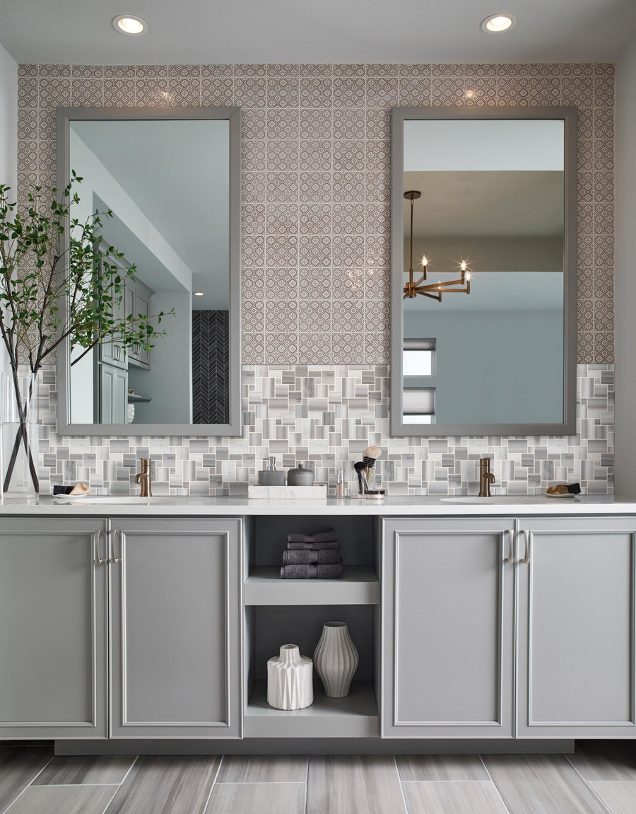 Modern bathroom with two large mirrors above a gray double-sink vanity, open shelves, and a leafy branch in a vase. The sophisticated look is completed by Magic Pattern Mosaic Natural Stone tiles as the patterned backsplash.