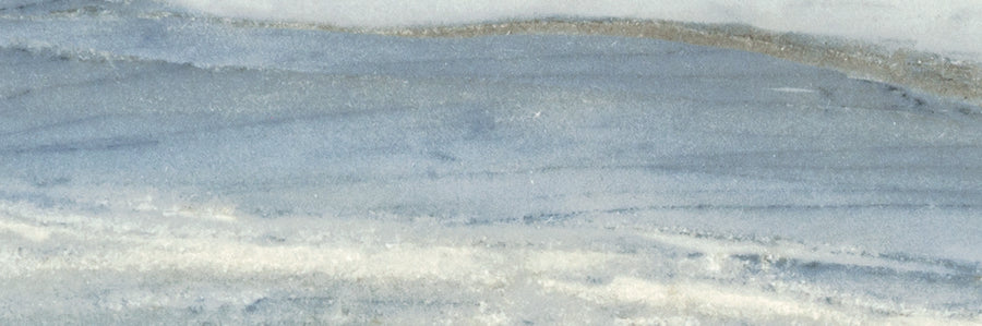 A close-up of the Monte Carlo 4x12 Porcelain Tile highlights its smooth surface with light blue, white, and gray swirls, showcasing a luxurious look reminiscent of polished marble or natural stone.