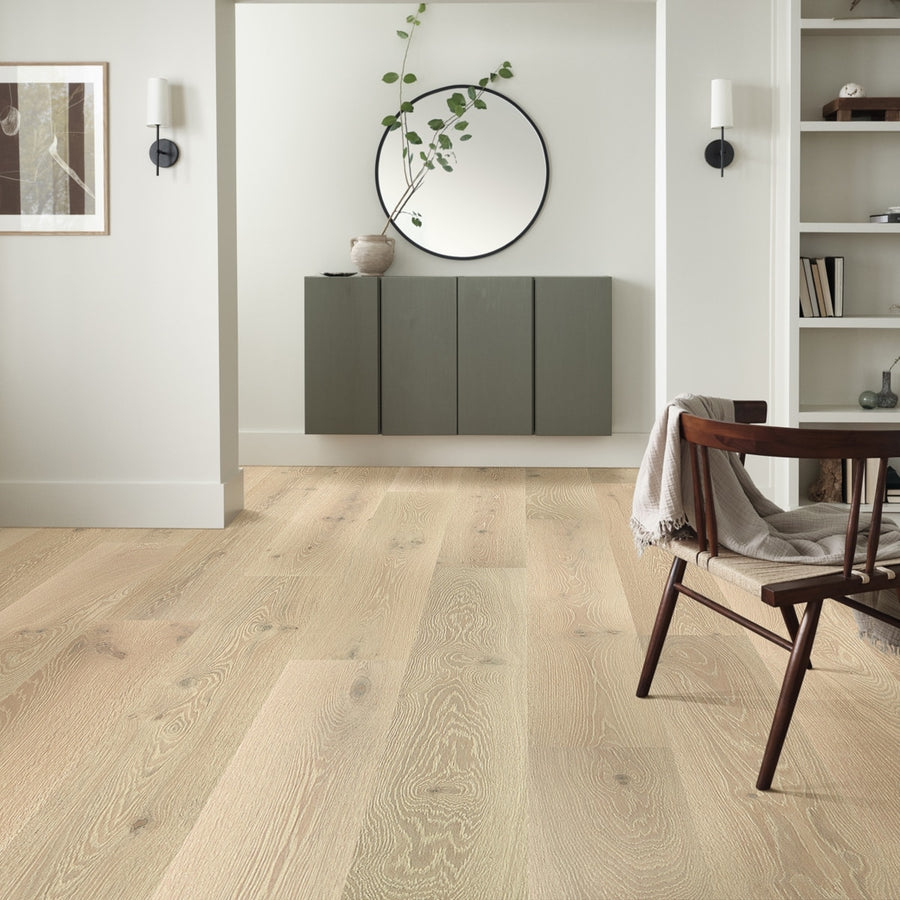 Minimalist living space with light wood flooring, a wall-mounted green cabinet, round mirror, and simple decor. The dining area features Monticello 8 1/2" White Oak Hardwood floors and a modern chair draped with a blanket.