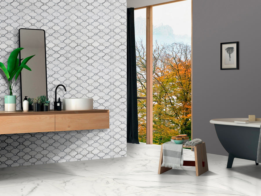 Modern bathroom with a Moroccan Braid Honed Waterjet Mosaic accent wall, wooden vanity, round sink, black faucet, and large mirror. A freestanding tub sits by a floor-to-ceiling window with autumn views. Marble floor and gray walls included.