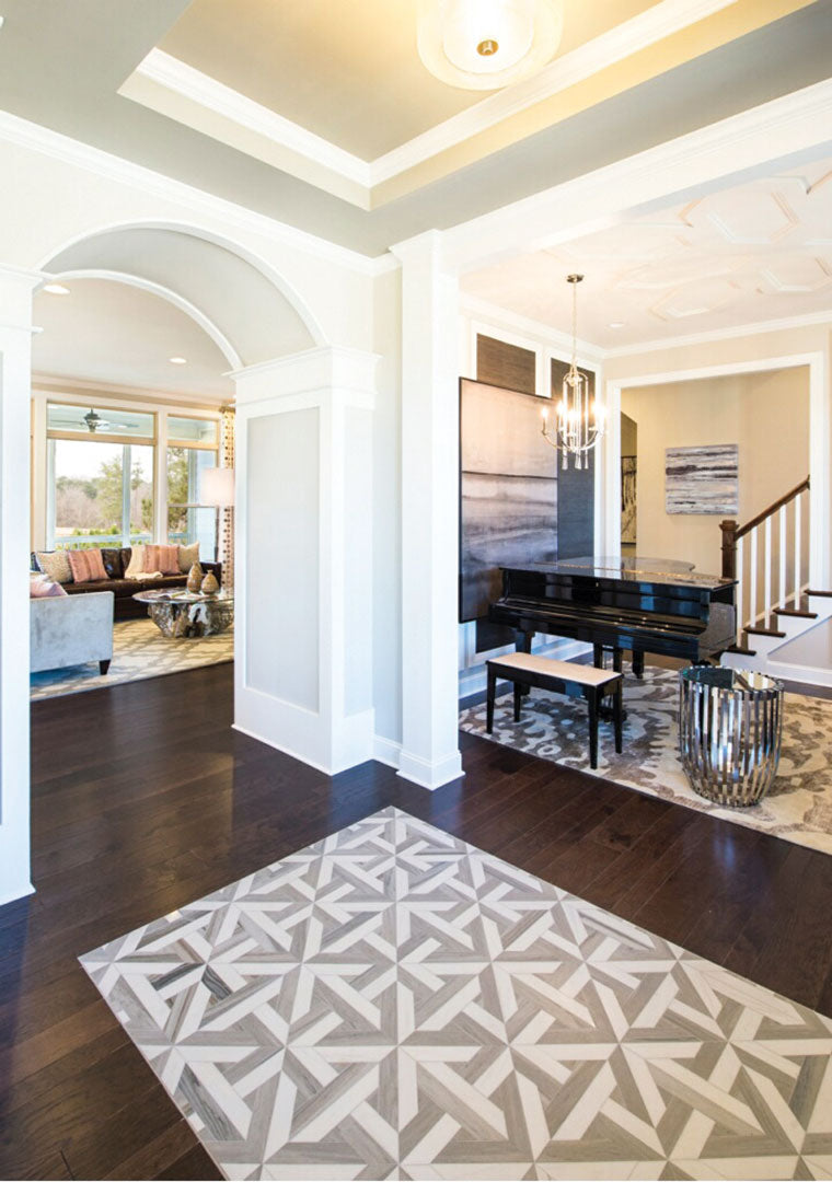 Bright, elegant entryway features modern Talya Rubicon Skyline 17x17 3/8 Waterjet Natural Stone tiles, dark wood flooring, a black grand piano on a rug, modern chandelier, and an arched doorway opening to a sunlit living room with large windows.