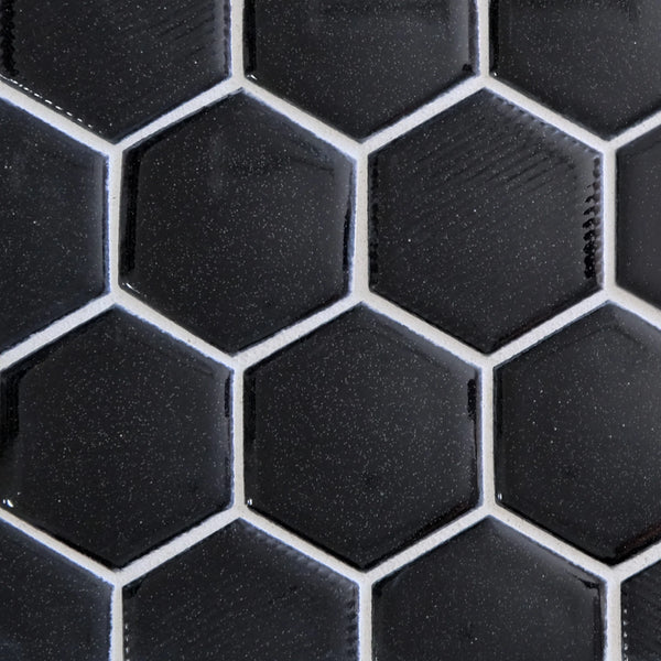 Close-up of New Form Hexagon Mosaic Tile in black, featuring glossy hexagonal pieces with white grout lines. The subtle texture and reflective finish create a striking honeycomb pattern, perfect for shower walls or kitchen backsplashes.