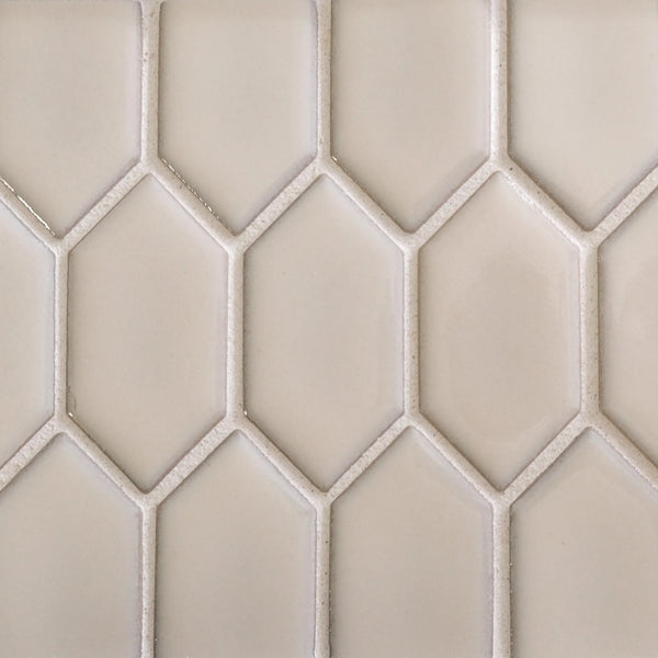Close-up of a beige shower wall with a geometric honeycomb pattern, featuring New Form Picket Mosaic Tile. The elongated hexagonal tiles are separated by light grout lines, and the surface appears smooth and glossy.