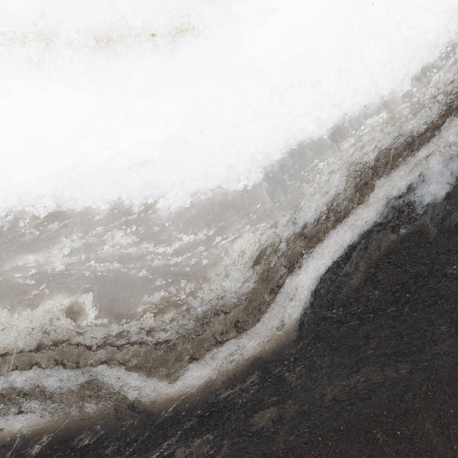 Close-up view of a snowbank with layers of white snow, gray ice, and dark ground—its textured, stratified appearance is reminiscent of in-stock choices like Opus 8x8 Rectified Ceramic Tile with its modern finish.