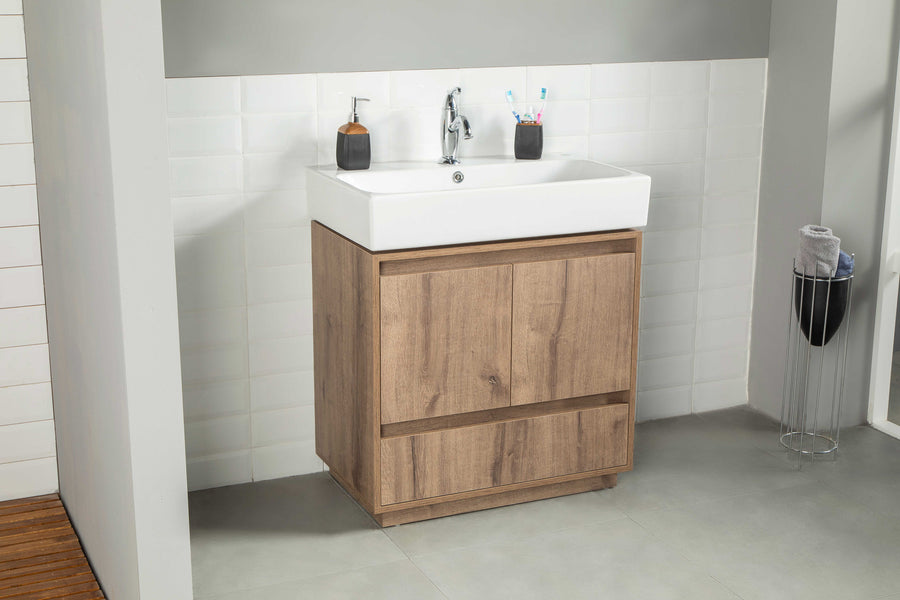 The Romina 30" Vanity includes a white rectangular sink, chrome faucet, and wooden cabinet, topped with a soap dispenser and toothbrush holder, all set against white tile walls and gray floors for a modern look.