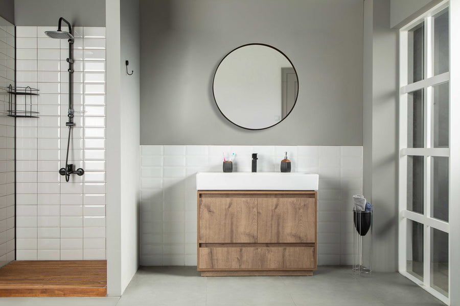 A modern bathroom with a walk-in shower on the left, a Romina 39" Vanity with soft-close drawers and white sink in the center, two toothbrushes on top, round mirror above, and a window on the right letting in natural light.
