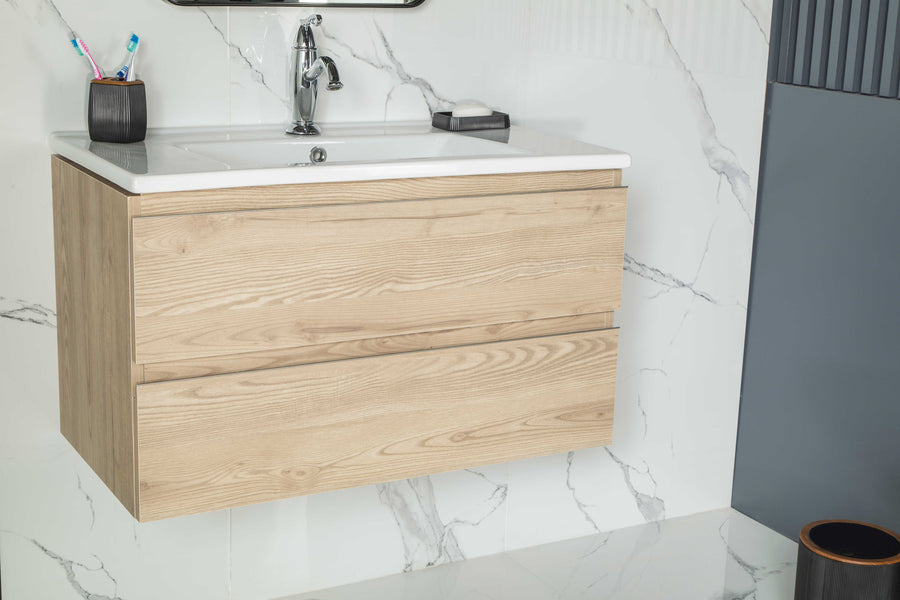 The Simena 30" Vanity features light wood soft-close drawers, a white sink, chrome faucet, toothbrush holder, and soap dish. Its wall-mounted design and white marble wall with grey veining add modern style and functionality to your bathroom.
