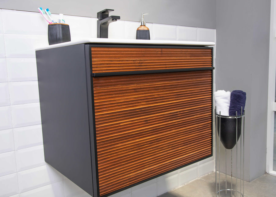 The Urban 24" Vanity pairs a white countertop with a black and wood-textured cabinet for an industrial look, complete with a black faucet, soap dispenser, toothbrush holder, metal towel stand, and sleek white tiled wall backdrop.