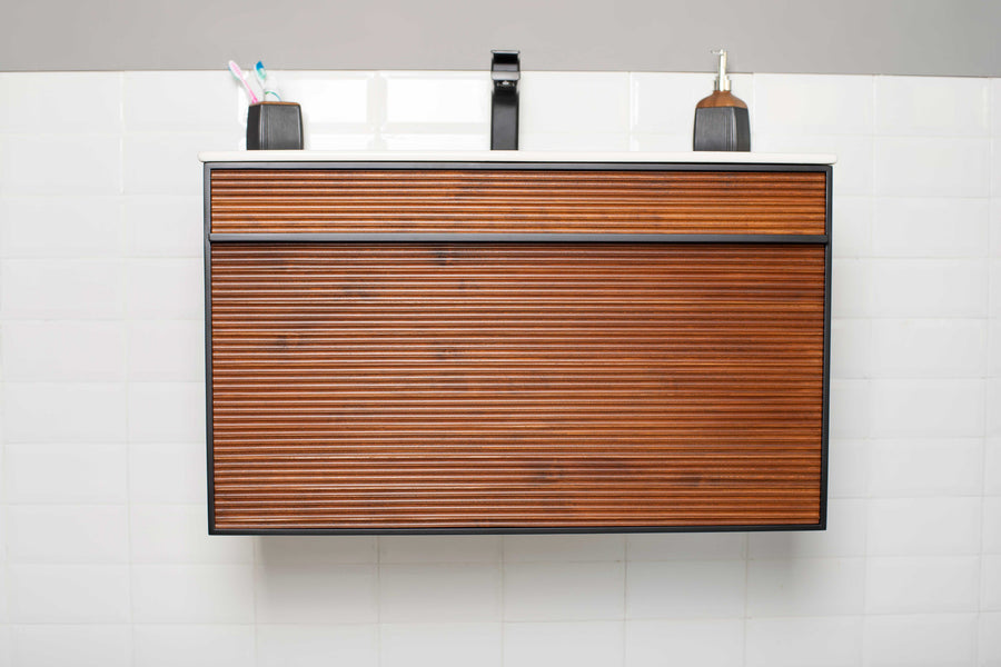 The Urban 36" Vanity features a textured wooden drawer, white countertop, black faucet, soap dispenser, and toothbrush holder with three toothbrushes for a modern look against a white tile wall.