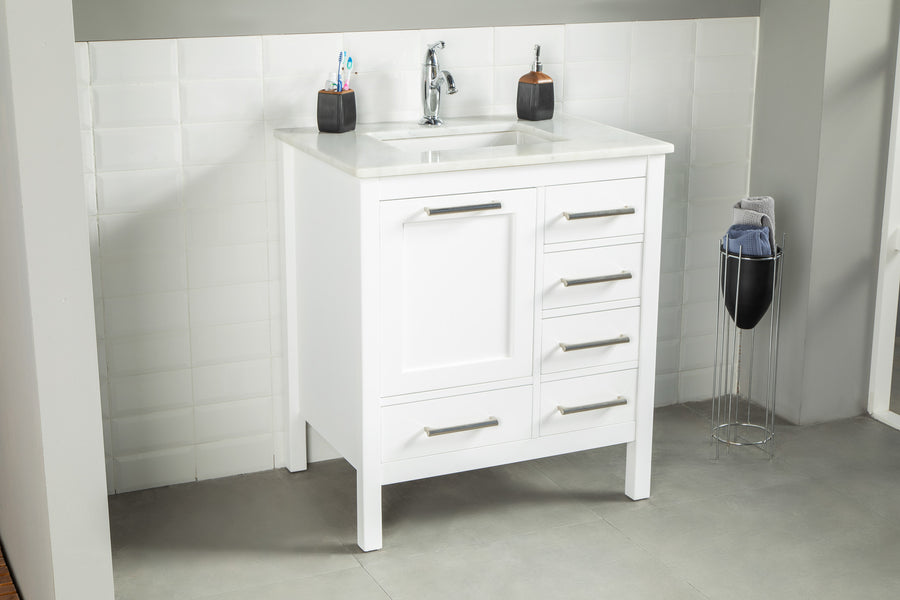 The Ashley 30" Vanity in natural oak features a sink, silver faucet, and four drawers. Set on gray tile flooring with white tiled walls, it's complemented by a soap dispenser, toothbrush holder, and towel stand nearby.