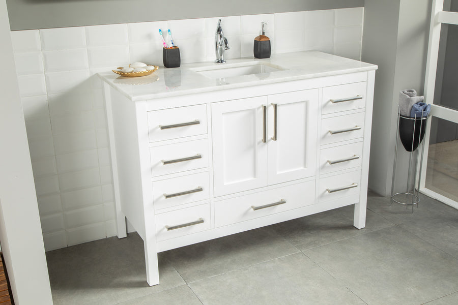 The Ashley 48" Vanity features a modern white finish with silver handles, white countertop, integrated sink, soap dish, and cup with two toothbrushes. It stands out against gray floor tiles and a white tiled wall.