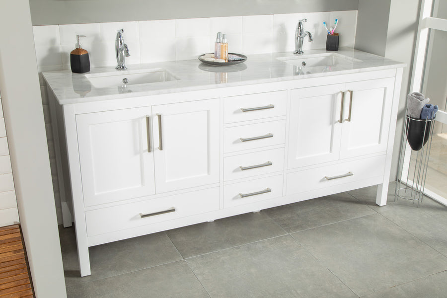 The Ashley 72" Double Bowl Vanity features a modern white finish, soft-close drawers with silver handles, a marble countertop, and is styled with soap dispensers, toothbrushes, toiletries on a tray. Tiled floors and walls; towel stand on the right.