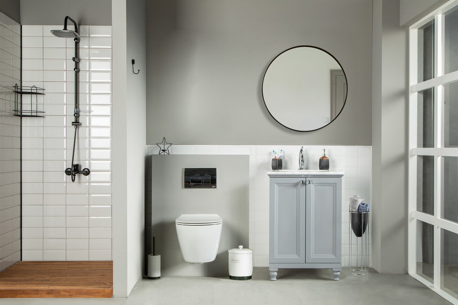 Modern bathroom with an Isabel 24" Vanity featuring solid wood drawers, a walk-in shower, wall-mounted toilet, mirror above the vanity, neutral minimalistic decor, plus a small trash can and magazine holder beside the vanity.