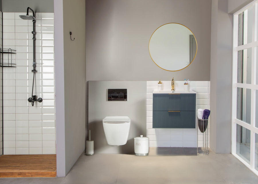 Modern bathroom with a walk-in shower on the left, wall-mounted toilet in the center, and a Sorrento 24" Vanity under a round mirror. Soft-close drawers and gold faucet add elegance as natural light highlights every detail.