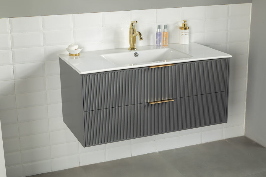 The Sorrento 36" Vanity boasts a ribbed gray cabinet, white countertop, gold faucet and handles. Set against white tiled walls, it’s an ideal modern bathroom upgrade. Toiletries and a soap dispenser sit neatly on the countertop.