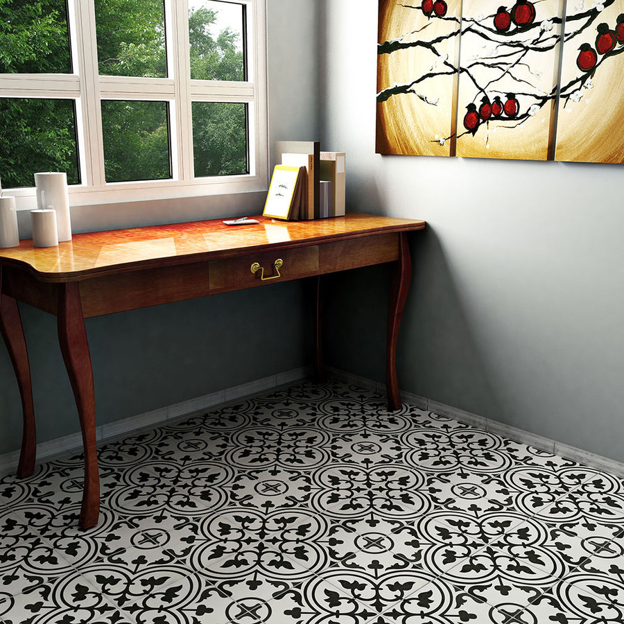 A wooden desk with papers and white vases sits by a window with greenery, while the room showcases Arte 9 3/4 x 9 3/4 Patterned Tile on the floor and wall, plus a wall art piece featuring red and black branches.