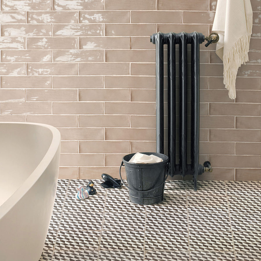 A bathroom featuring Kings Espiga 17 3/4 x17 3/4 Patterned Tile on the floor, beige brick-style wall tiles, a black radiator with a white towel, and vintage-industrial accents by a white bathtub.