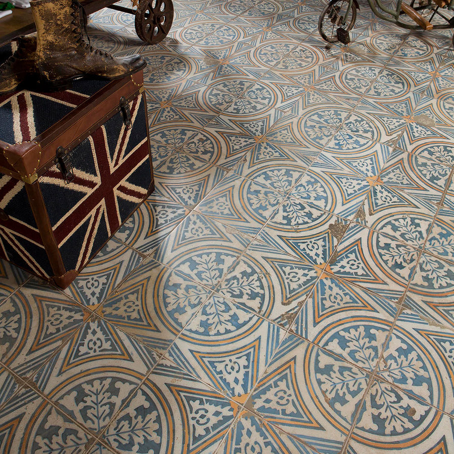 Kings 17 3/4 x17 3/4 Patterned Tile features blue, beige, and gray floral and geometric patterns. A Union Jack chest and vintage metal cart complete the space’s eclectic, industrial vibe.
