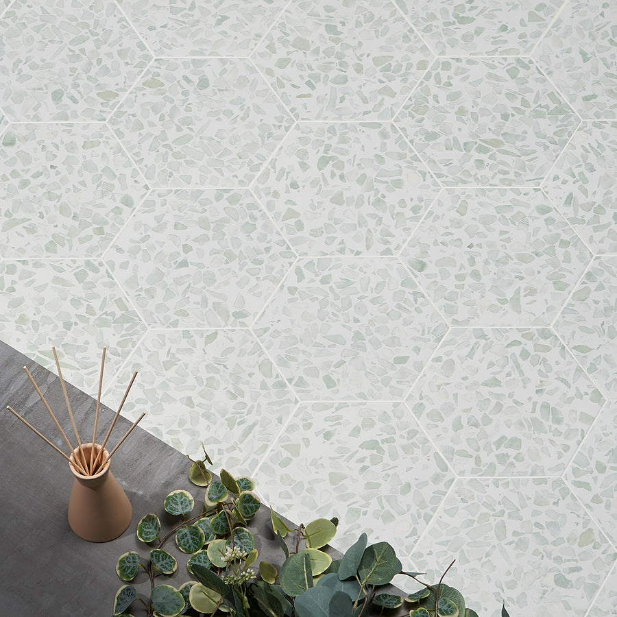 A plant beside a vase sits atop Riazza 9" Hexagon Porcelain Tile, lending a modern touch to the space.