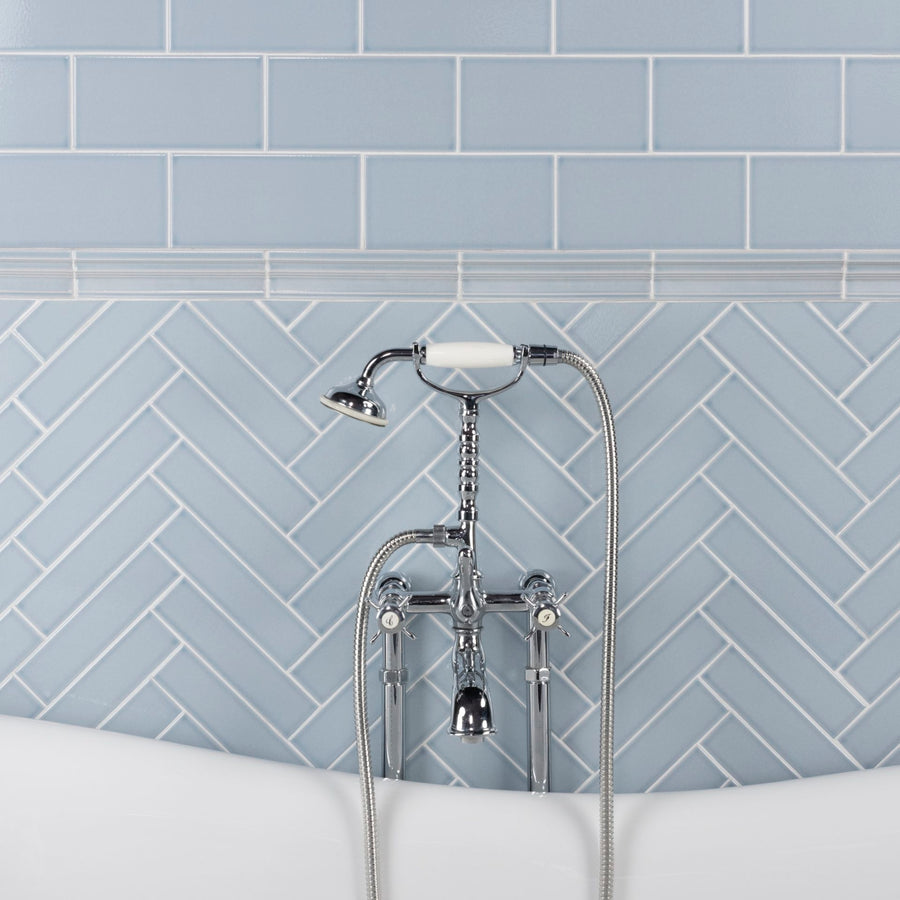 A bathtub with a chrome faucet and handheld shower head is set against a wall clad in Scandia 2x8 Crackle Finish Subway Tile; the upper section is laid horizontally, while the lower section uses a herringbone pattern.